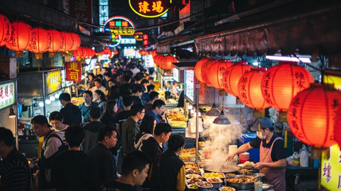 A photo capturing the vibrant street life of a night market in Taipei. The scene